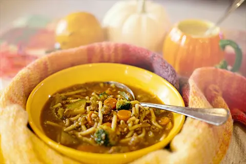 bowl of lovage leaves soup with noodles and vegetables wrapped in a warm scarf