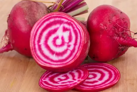 chioggia beet sliced rings with whole red beets on a wooden cutting board